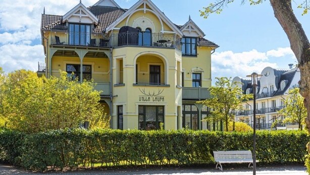 Un edificio amarillo con balcones y un letrero que dice 'Villa Laura'.