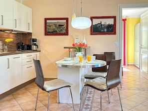 A kitchen with white cabinets, a dining table with chairs, a coffee maker, and a vase with flowers. - (210) 2-room apartment - apartment house Villa Laura (Kühlungsborn)