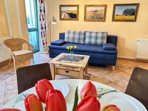 A living room with a blue sofa, a coffee table, and a dining table set for two. - (210) 2-room apartment - apartment house Villa Laura (Kühlungsborn)