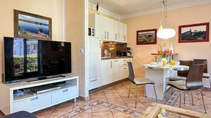 Una sala de estar con televisor, un comedor con mesa y sillas, una cocina con armarios y piso de baldosas.