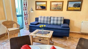 Una sala de estar con un sofá azul, una mesa de centro y una mesa de comedor para dos.