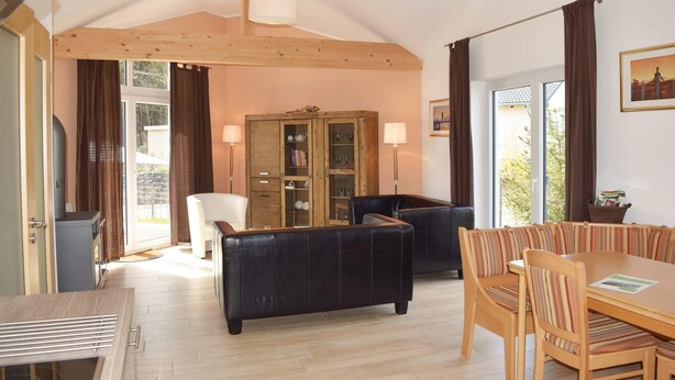 A cozy living room with a black sofa, a wooden dining table, and a cabinet with glass doors. - Amazing home in Gerolstein with kitchen (Gerolstein)