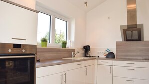 A modern kitchen with white cabinets, a stainless steel oven, a coffee maker, and a window with potted plants. - Amazing home in Gerolstein with kitchen (Gerolstein)