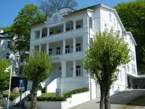 A white building with a central entrance, multiple windows, and a sign with a 'Q' logo.