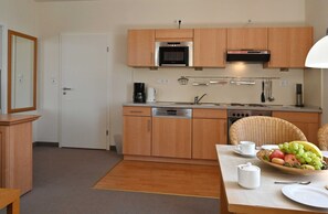 A compact kitchen with wooden cabinets, a microwave, a coffee maker, and a dining area with a fruit bowl and plates.