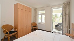 Un dormitorio con cama, armario, silla y balcón con vistas.