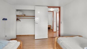 Een kamer met twee houten bedden, een kledingkast en een deur naar een andere ruimte.