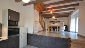 Eine moderne Küche mit integrierten Geräten, einer Wand aus Naturstein und einer Holztreppe, die in einen Essbereich führt.