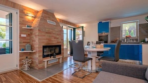 A modern living room with a fireplace, a dining area, and a kitchen with blue cabinets.