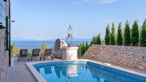 A swimming pool with a stone wall and a view of the sea.