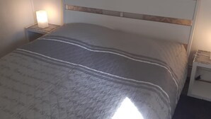 Un letto rifatto con copripiumino trapuntato e una testiera, due comodini con lampade, e una carta da parati decorata al muro.