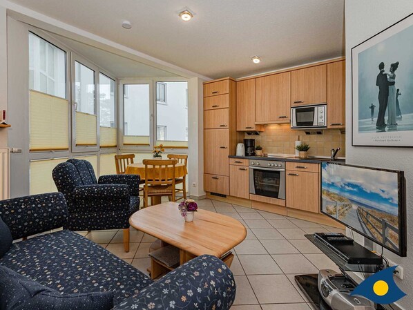 Un espace de vie compact comprenant un coin repas, une kitchenette et un espace détente avec vue sur l’extérieur.
