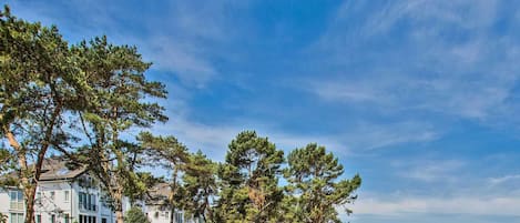 A coastal residential area with multi-story buildings, dense greenery, and a clear view of the sea.