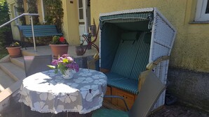 Un espace extérieur aménagé avec une table ronde, une chaise en osier et une petite table sur laquelle est posé un vase de fleurs.