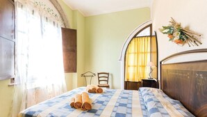 A room with a checkered bedspread, a wooden headboard, a chair, and a window with curtains. - Beautiful apartment in Pomarance (Pomarance)