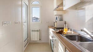 A modern kitchen with white tiles, a built-in oven, a microwave, a kettle, and a sink.