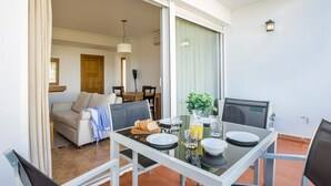 A dining area with a glass table, chairs, and a view of a living room with a sofa and a dining table.