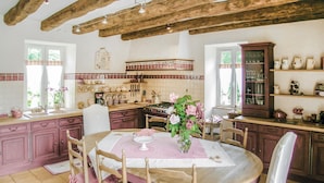 Une cuisine avec des poutres en bois, une table à manger avec des chaises roses et un buffet contenant de la verrerie.