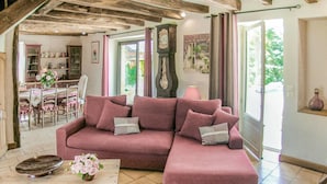 Un salon chaleureux avec un grand canapé d’angle rose, une table basse en bois surmontée d’un vase décoratif, et un coin repas avec des chaises et une table en bois.