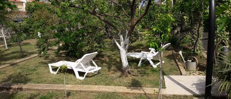 A garden with two white lounge chairs and a tree.