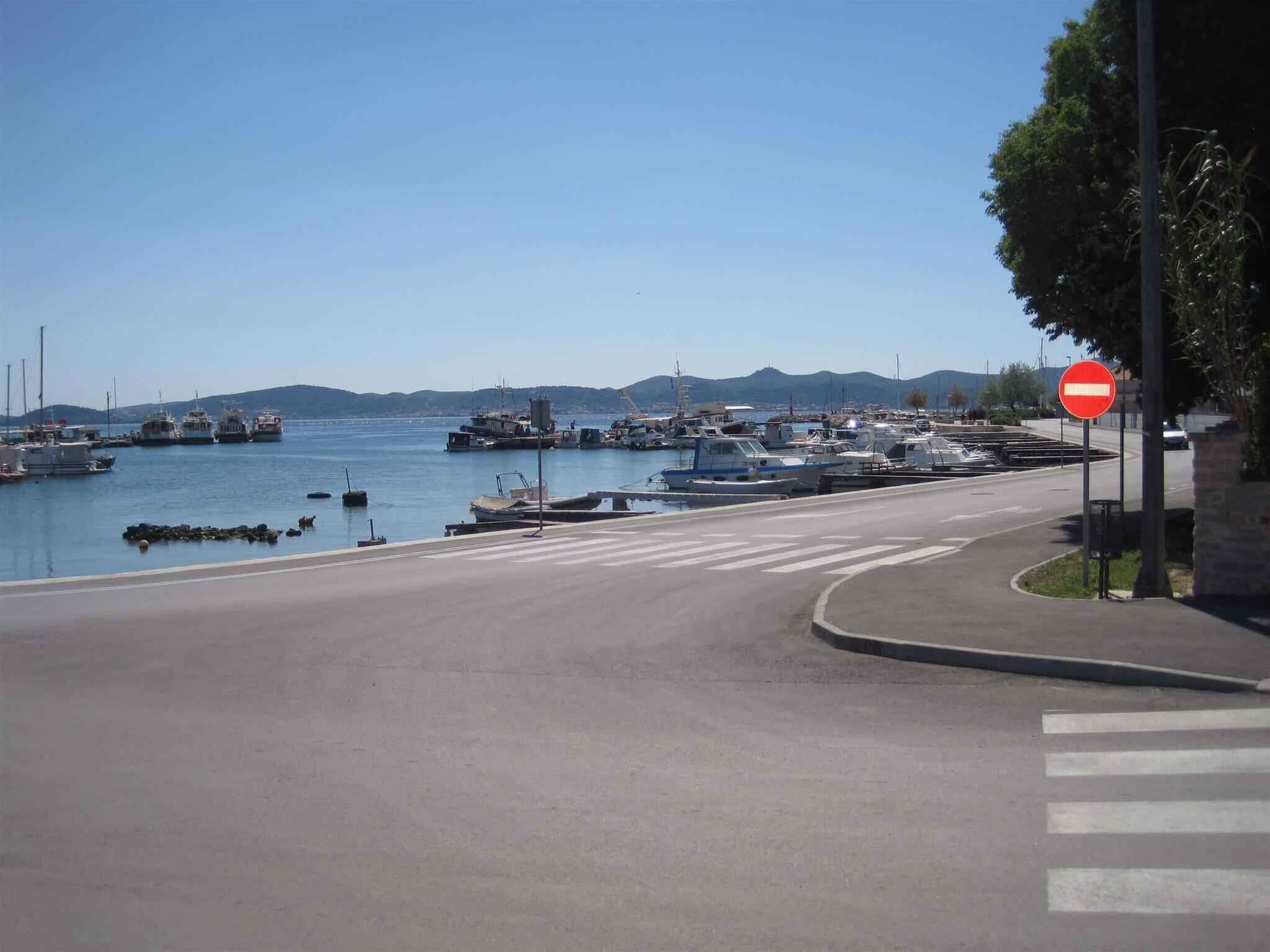 Une route côtière avec un panneau indiquant l’interdiction d’accès, un ciel dégagé et des bateaux amarrés dans une marina.