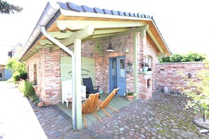 En murbygning med en overdækket veranda, en blå dør og to træstole.