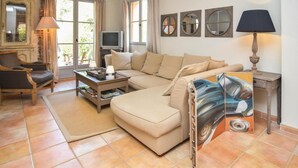 Una sala de estar con un sofá color crema, una mesa de centro de madera, un televisor y un cuadro en la pared.