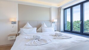 Une chambre d’hôtel avec un grand lit, deux lampes de chevet, une table de nuit et une fenêtre donnant sur des arbres.