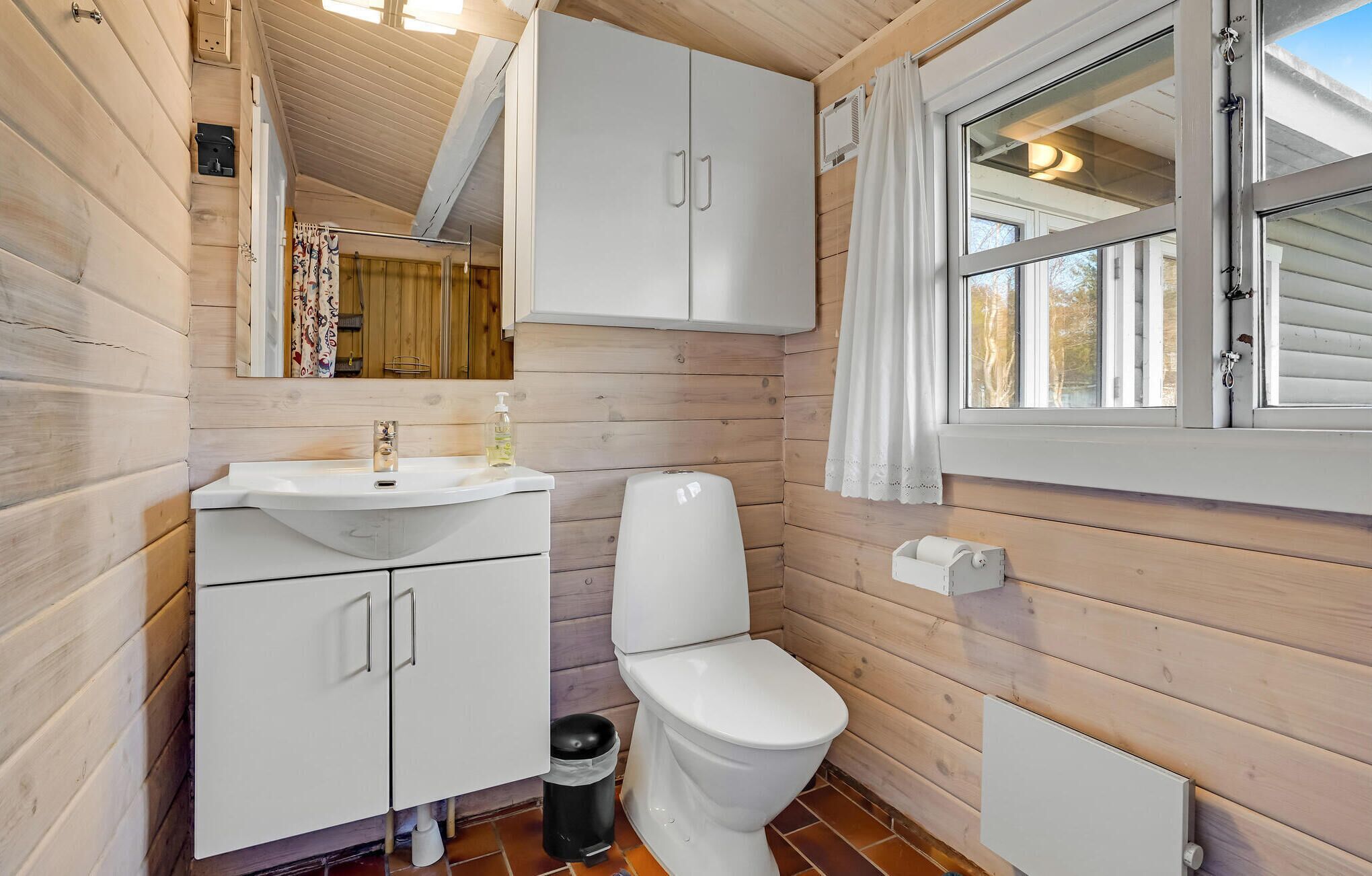 A compact wooden cabin bathroom with a white sink, toilet, and cabinets.