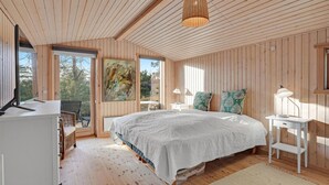 Ein Schlafzimmer mit einem großen Bett, einem Schreibtisch und einem Sessel. Ein Fenster bietet Blick auf Bäume.