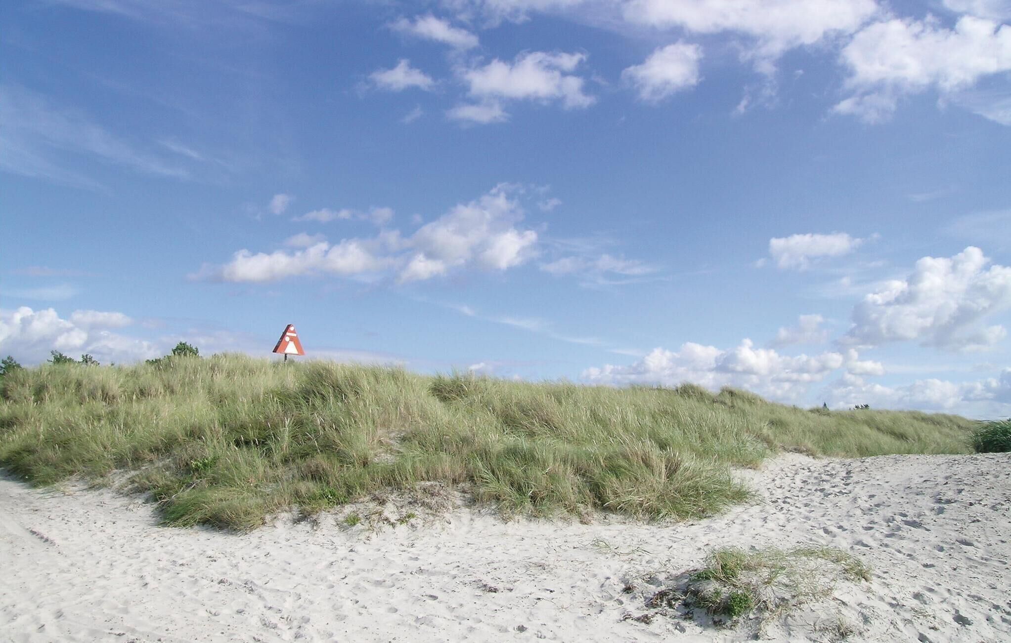 Une plage de sable avec une dune et un panneau indiquant la direction du vent.