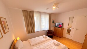 Una habitación de hotel con una cama, televisión, una silla, armario y puerta.