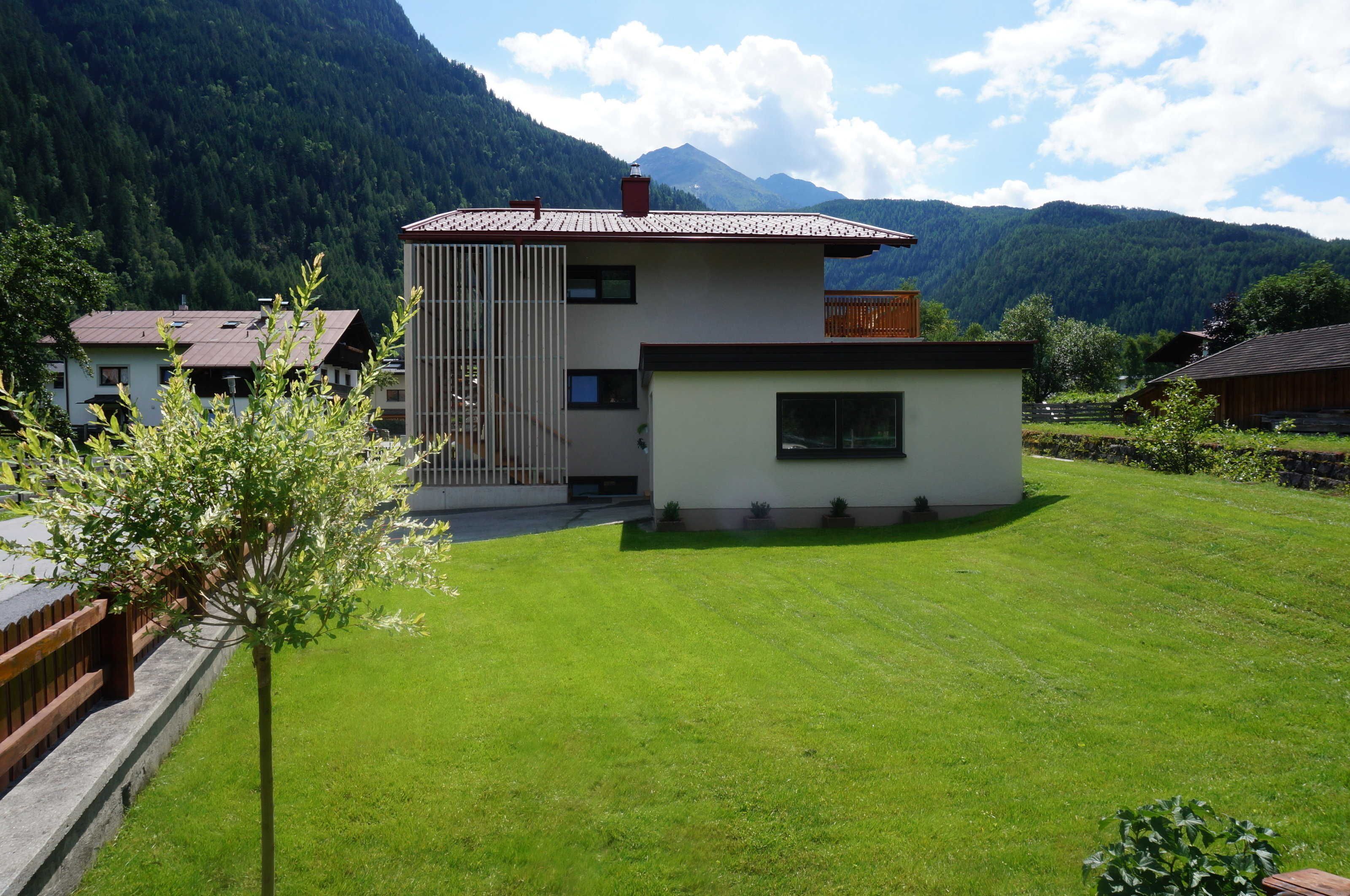 A modern two-story house with a small attached garage, surrounded by a well-maintained lawn and a mountain backdrop.