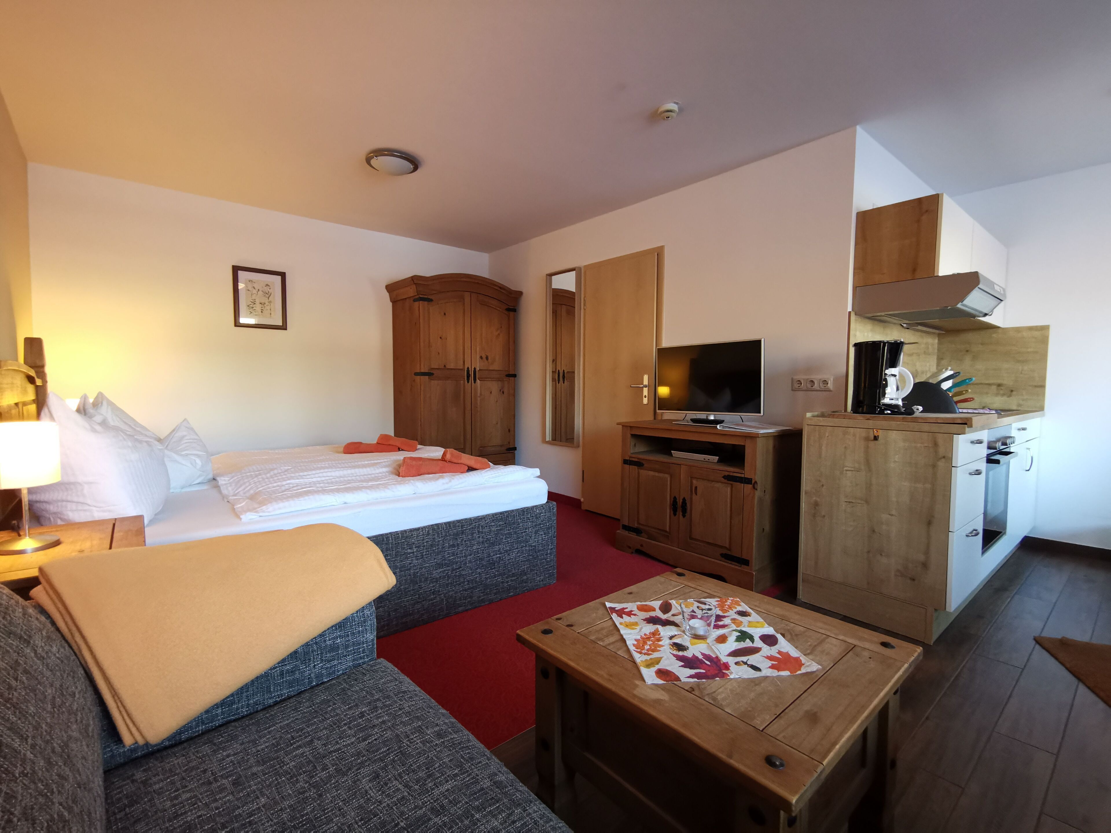 Une chambre d’hôtel comprenant un lit, un canapé, une petite table avec un set de table, une télévision, une kitchenette et une armoire.