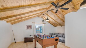Et værelse med trælofter, en ventilator, et fodboldbord, en sofa og et vindue med gardiner.