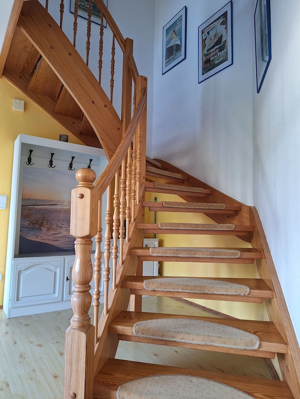 A wooden staircase with a handrail, carpeted steps, and a door at the bottom leading to a room with a white cabinet and a painting.
