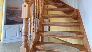 A wooden staircase with a handrail, carpeted steps, and a door at the bottom leading to a room with a white cabinet and a painting.