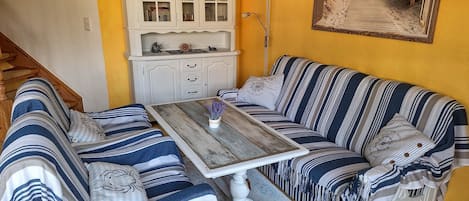 A room with a striped sofa set, a wooden table, a white cabinet, and a framed picture on the wall.