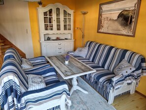 Een kamer met een gestreept bankje, een houten tafel, een wit kastje en een ingelijste foto aan de muur.