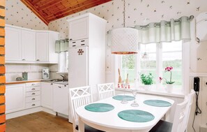 A kitchen with white cabinets, a refrigerator, a dining table with four chairs, and a hanging light fixture. - 2 bedroom cozy home in Lyrestad (Lyrestad)