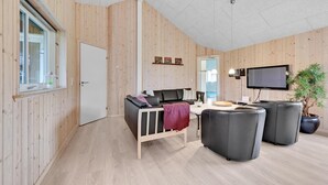 A modern, well-lit room with a wooden interior, a sofa, a TV, and a potted plant. - Stunning home in Tranekær with sauna (Tranekær)
