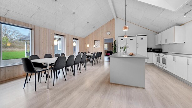 A modern kitchen with white cabinets, a central island, and a dining area with a long table and chairs. - Stunning home in Tranekær with sauna (Tranekær)