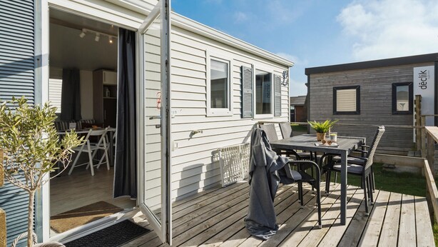 A mobile home with a deck, outdoor seating, and a small garden.