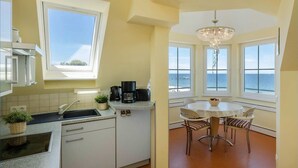 A kitchen with a coffee maker, a sink, and a window overlooking the sea. There is a dining area with a table and chairs. - Dune Residence A 20 - DR A 20 (Heringsdorf)