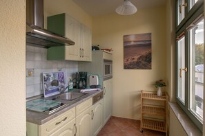 A kitchen with white cabinets, a stainless steel range hood, a coffee maker, and a window with a view of the outside.