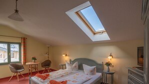 Une chambre avec un puits de lumière, deux lits simples, un bureau, des chaises, une commode et une petite table avec une lampe.