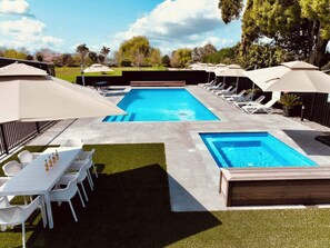 A swimming pool with two separate sections, surrounded by lounge chairs and umbrellas, with a table and chairs nearby.