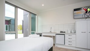 A modern hotel room with a large bed, a kitchenette, and a sliding glass door to the outside. - Podium Lodge (Cambridge)