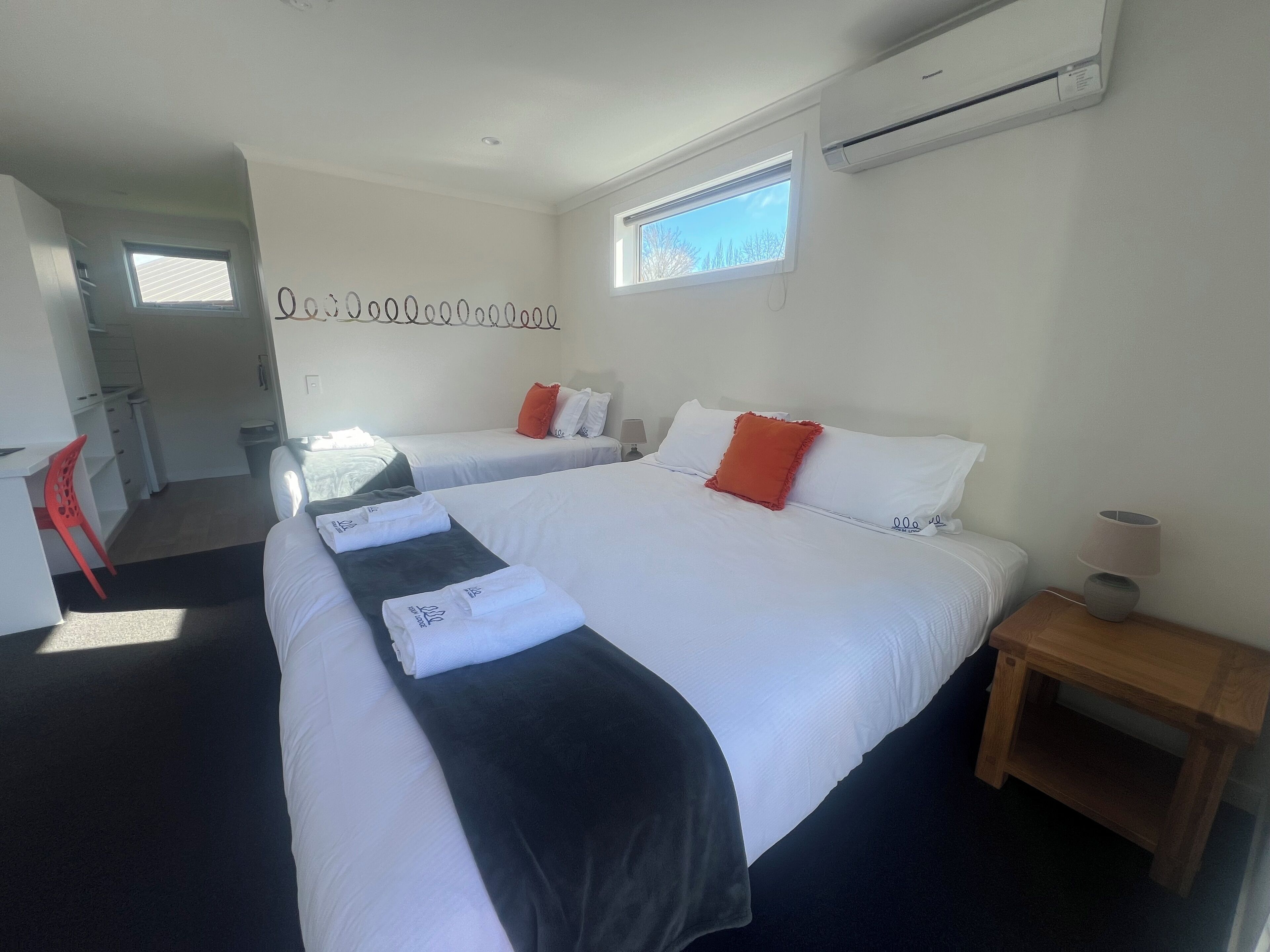 A hotel room with two beds, a desk, a chair, and a small table.