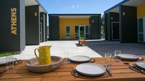 A modern building with numbered rooms, a dining area with tables set for two, and a clear sky. - Podium Lodge (Cambridge)